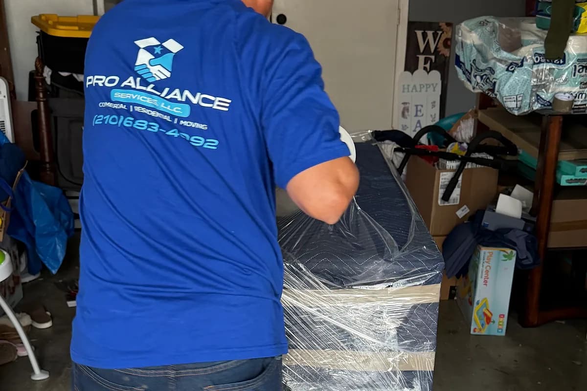 Pro Alliance mover carrying a shrink-wrapped dresser through a residential garage