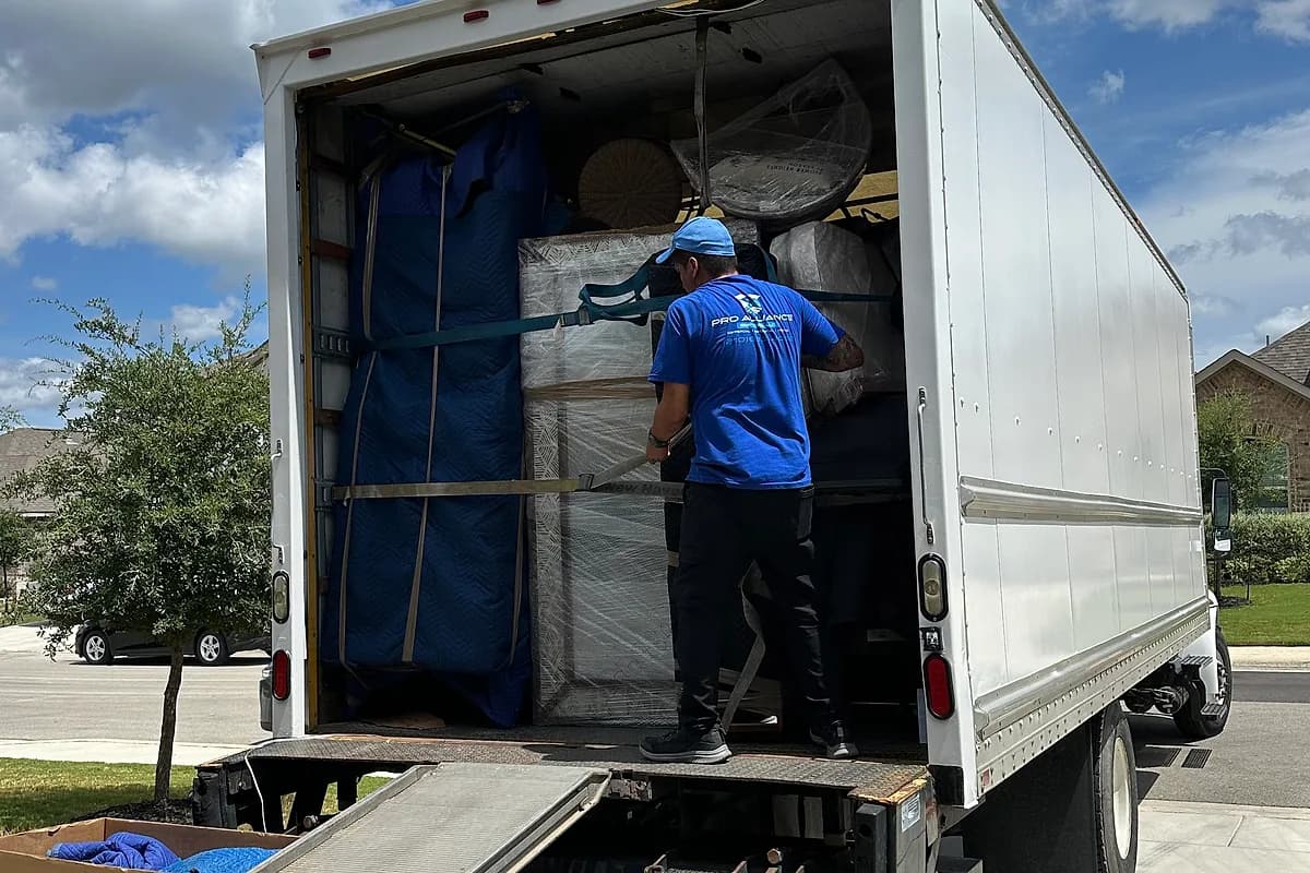 Pro Alliance Services crew loading a wrapped item into a box truck on a San Antonio residential street