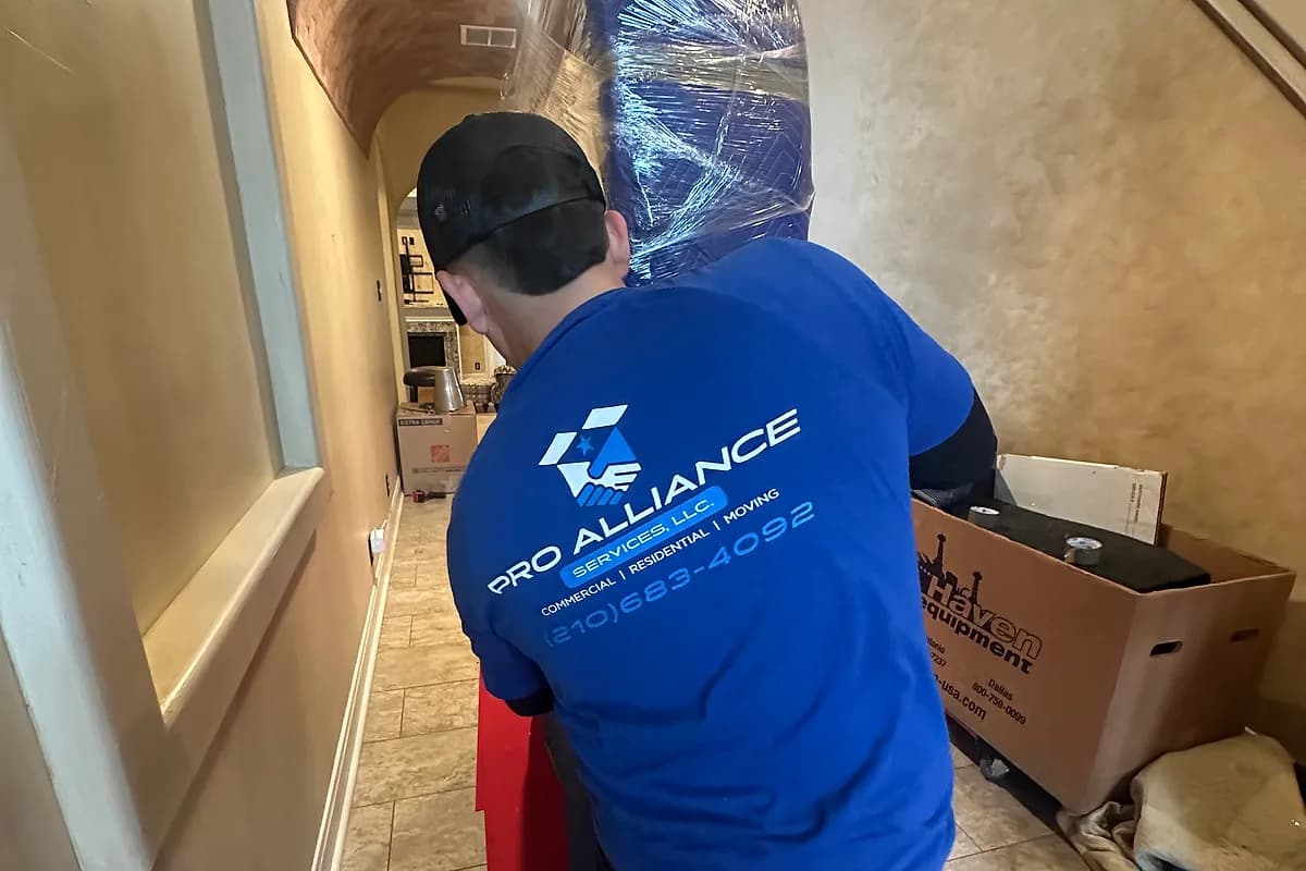 Pro Alliance mover carrying a shrink-wrapped headboard along a protected hallway runner