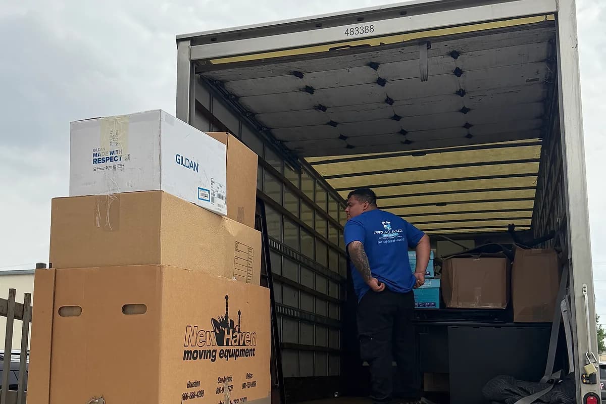 Pro Alliance mover loading cartons into a truck positioned inside a gated property entrance