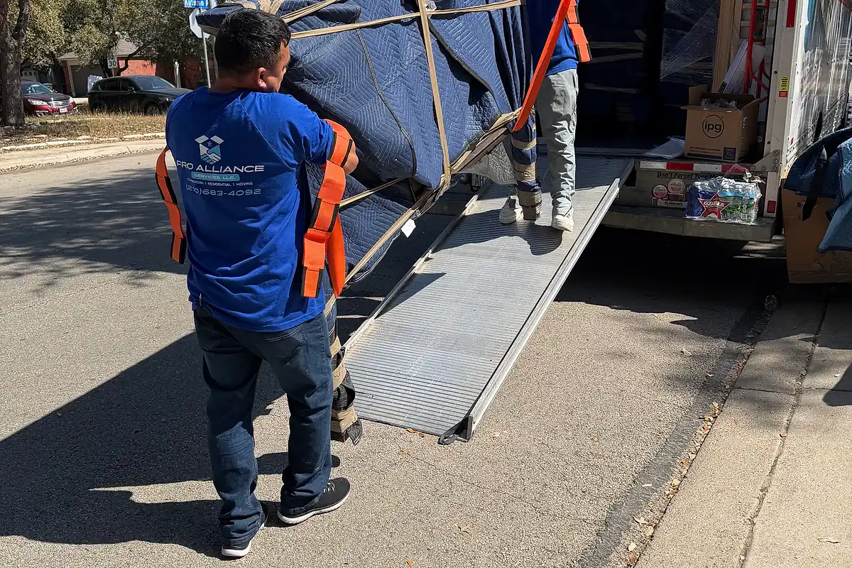 Two Pro Alliance movers guiding a blanket-wrapped piece up the ramp into a moving truck