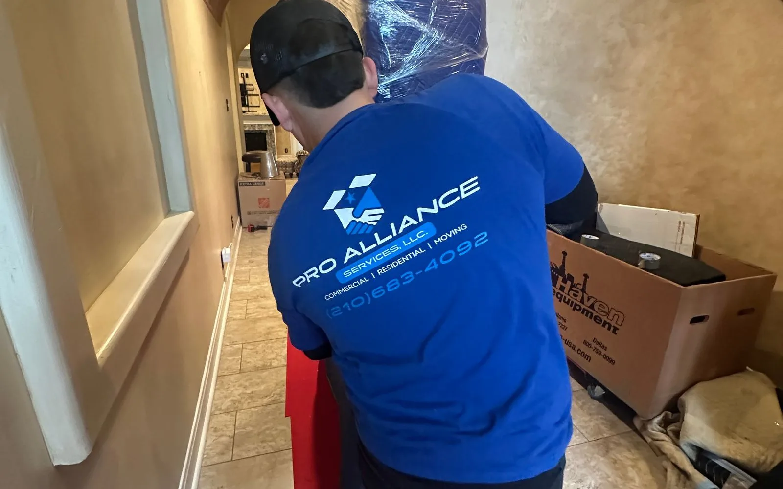 A Pro Alliance mover guiding a plastic-wrapped item along a hallway protected with a floor runner