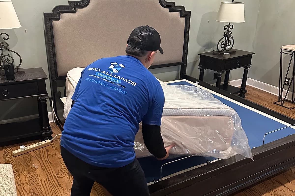 Pro Alliance mover wrapping a mattress and upholstered bed frame in protective material before transport