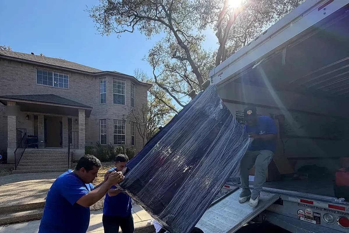 Pro Alliance movers guiding a tall shrink-wrapped piece down a ramp after clearing a tight interior route