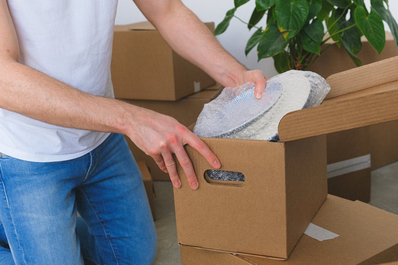 A person putting a items in the moving box in order to pack fragile items when moving to Converse
