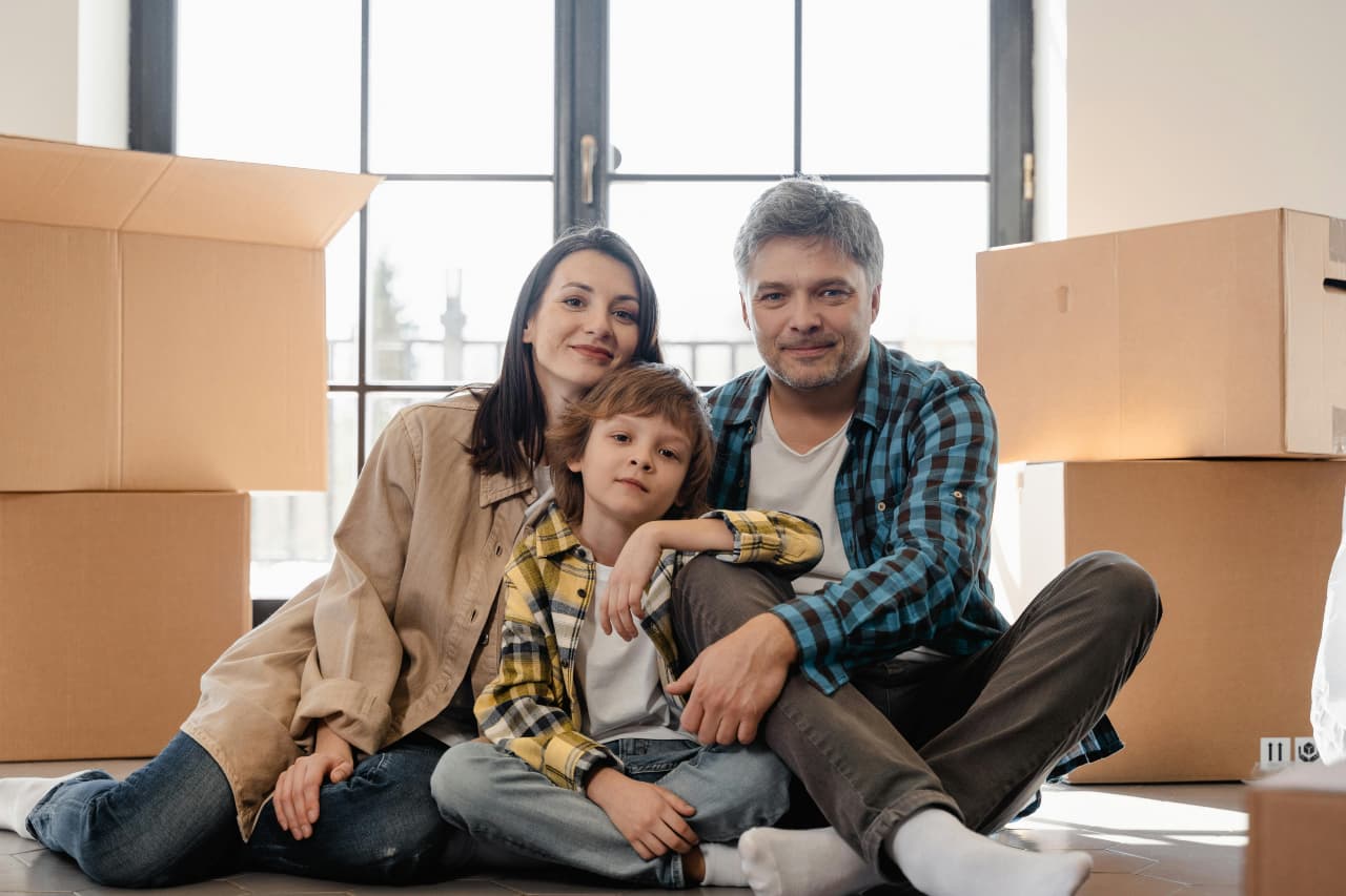 Happy family with parents and child sitting on the floor surrounded by moving boxes in their new home.