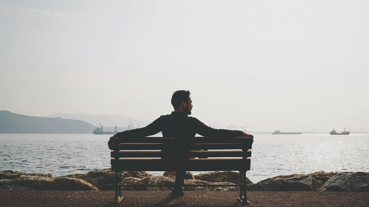 Man Sitting on Bench Near Body of Water