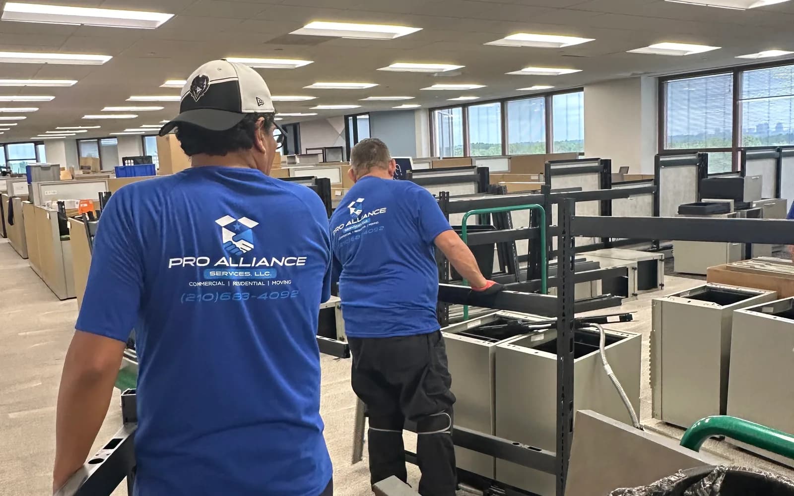Two Pro Alliance crew members break down cubicle workstations on an open office floor