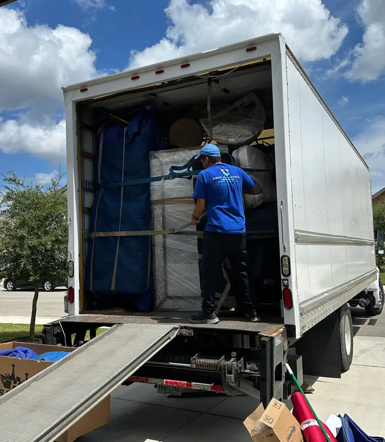 Pro Alliance mover securing a strapped, blanket-wrapped load inside the truck