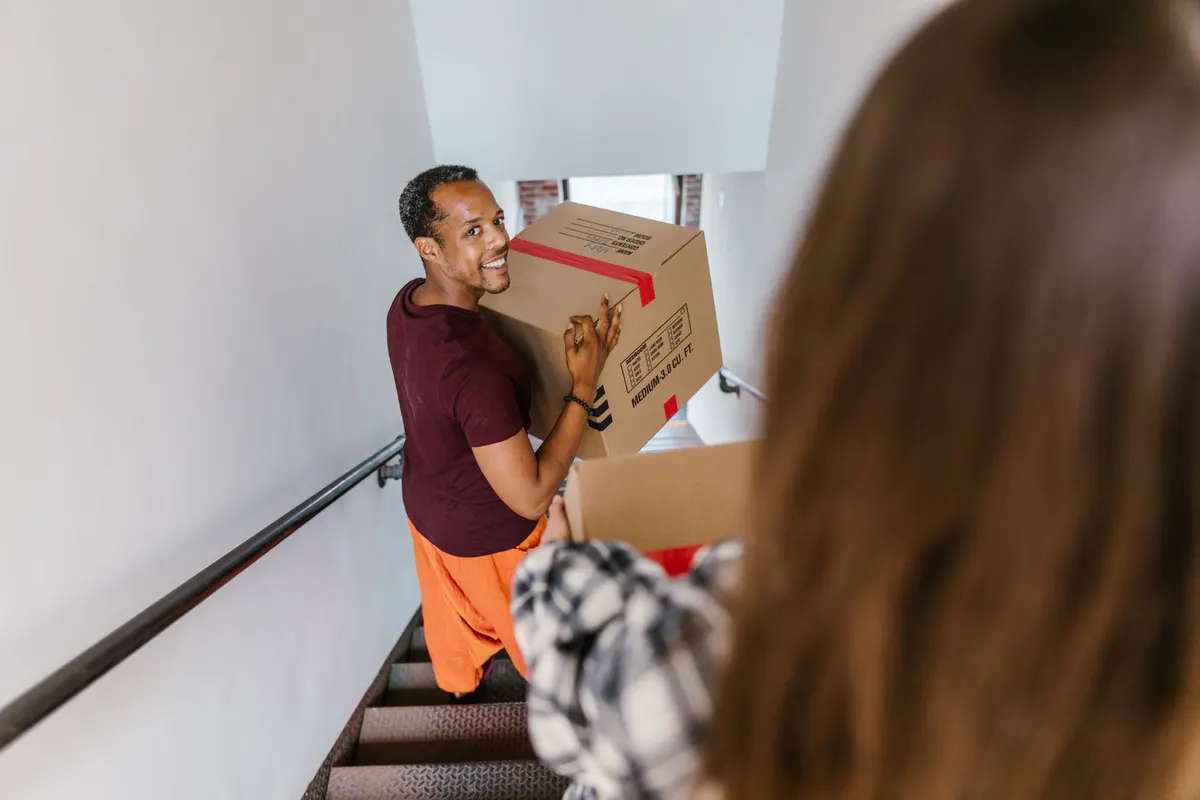 Person carrying a moving box up an interior staircase
