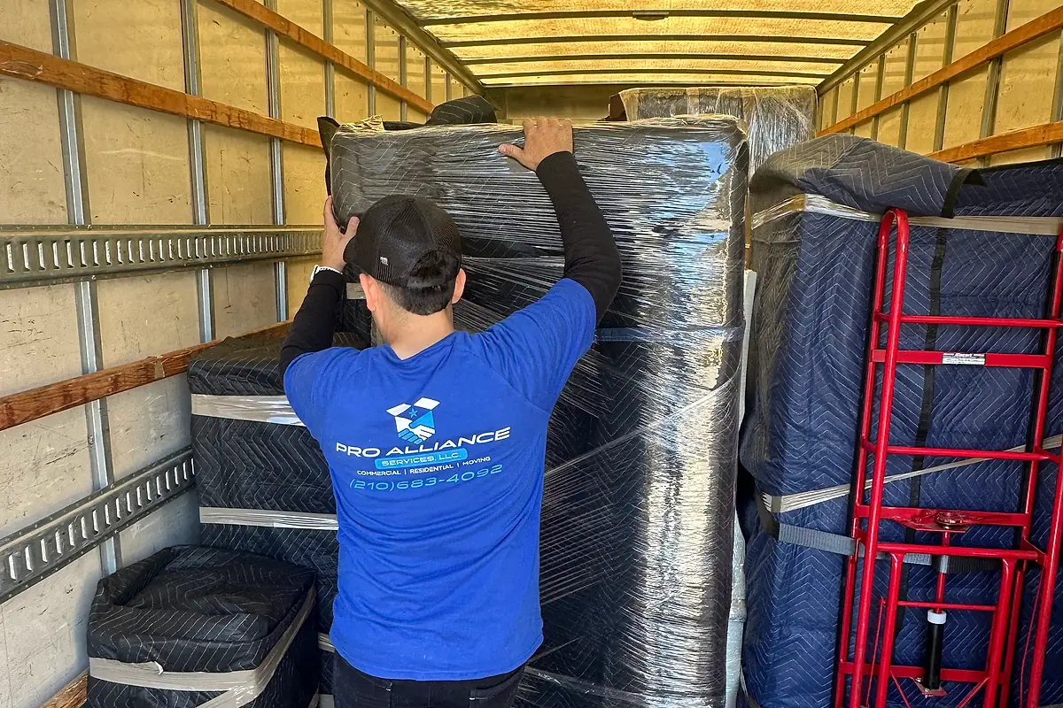 Pro Alliance mover securing a shrink-wrapped stack of furniture inside a loaded moving truck