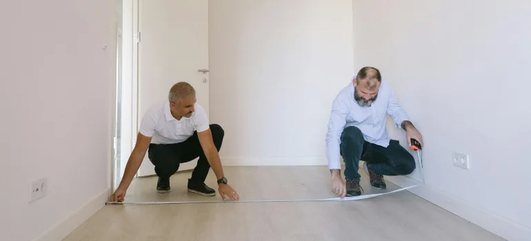 Two people cleaning the floor of an empty apartment