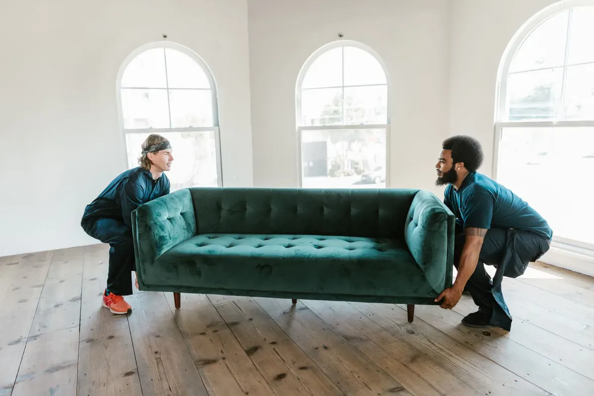 Two people carrying a sofa across a protected interior route