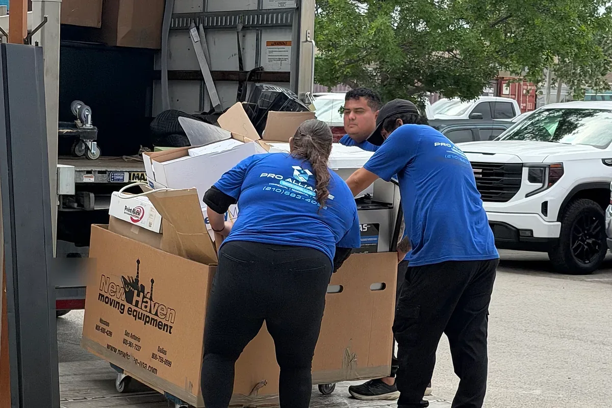 Two Pro Alliance movers lifting a packed container into a moving truck
