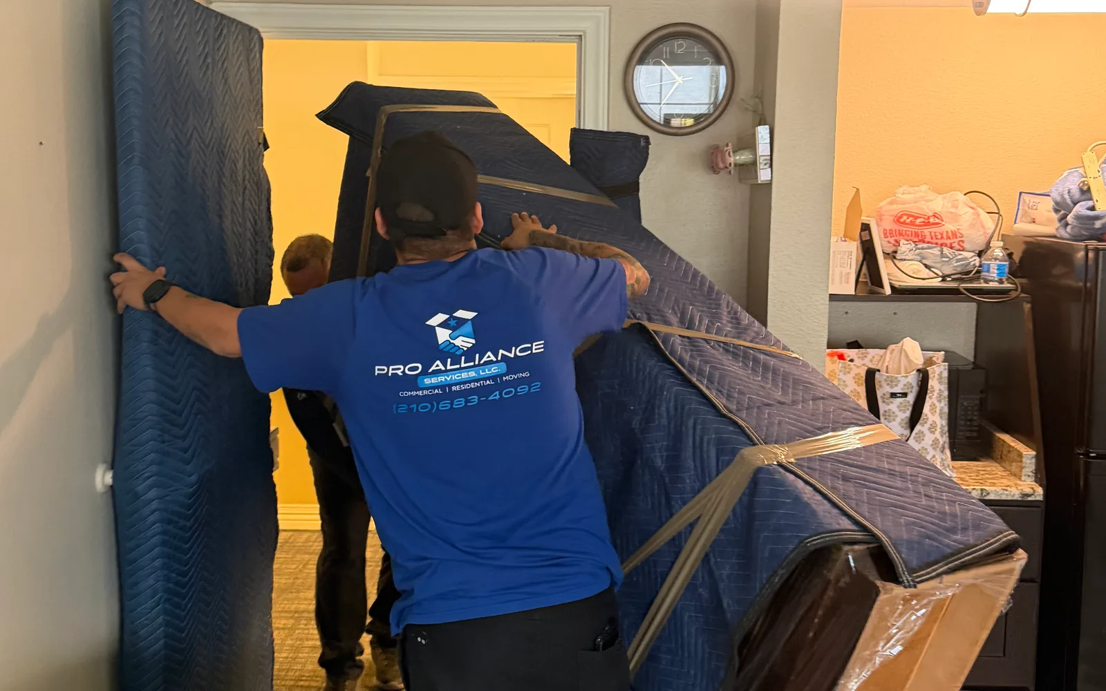Two Pro Alliance crew members moving a large padded furniture item through an interior doorway