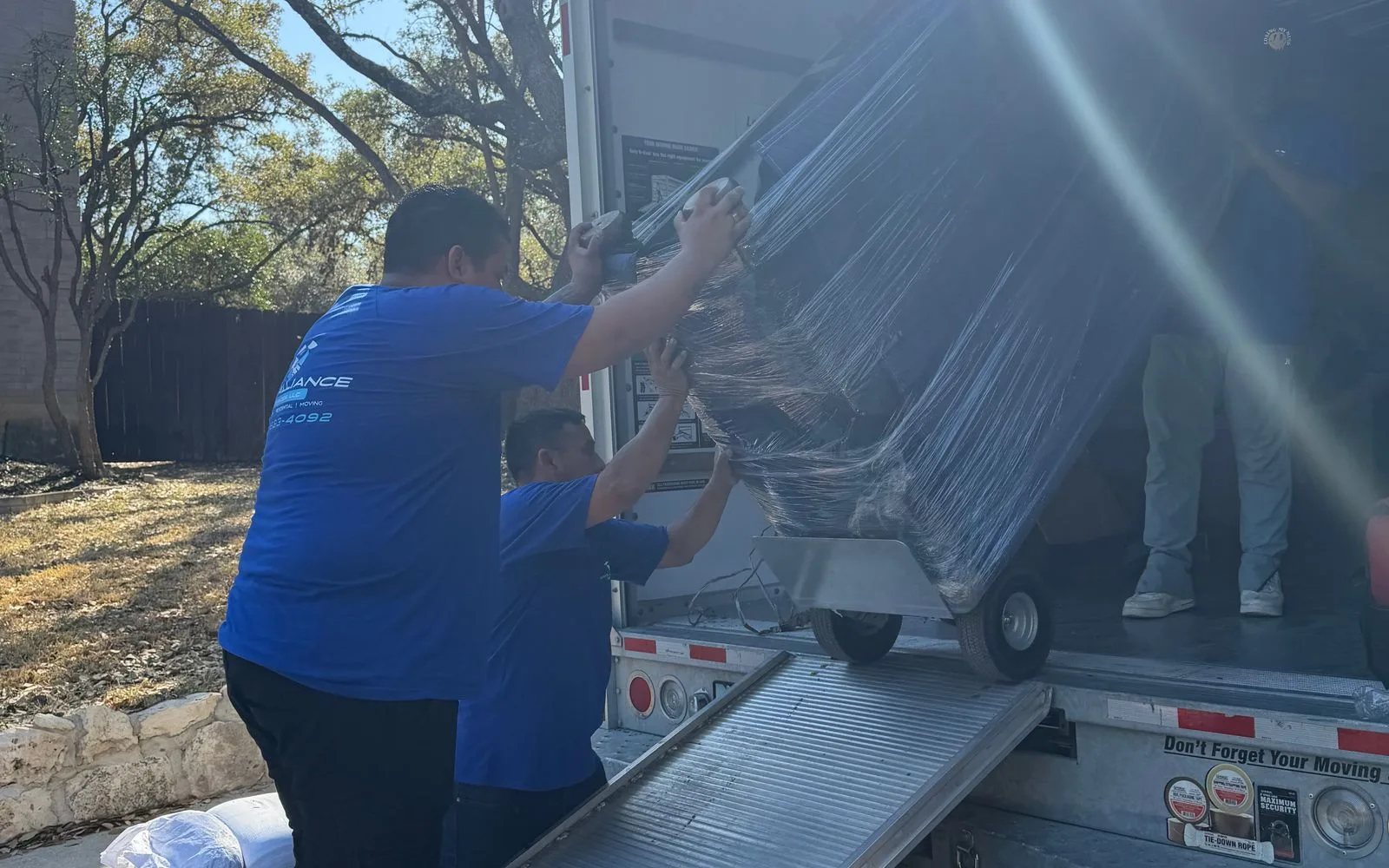 Pro Alliance crew members pushing a shrink-wrapped item on a dolly up a truck ramp