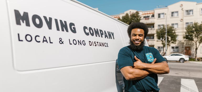 Smiling mover standing beside a van labeled "Moving Company" during a corporate relocation to Helotes.