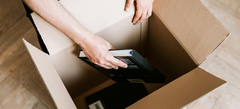Hands placing a hardcover book inside an open moving box.