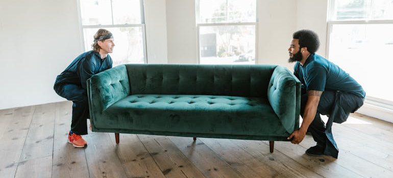Two men carrying a green sofa and placing it into a room.