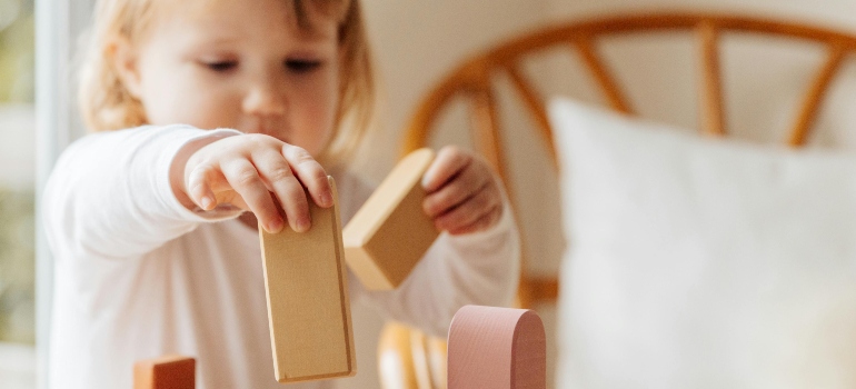 ChatGPT said:Little girl playing with wooden blocks at home while preparing kids for a relocation from Fredericksburg to Boerne