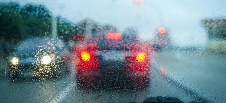 Blurry traffic seen through a rain-covered windshield during a move on a wet highway.