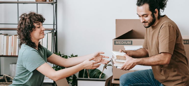 Couple placing books into a moving box while preparing their home for relocation.