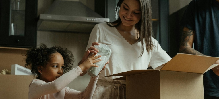 Parent and child placing a wrapped fragile item into a moving box in the kitchen.