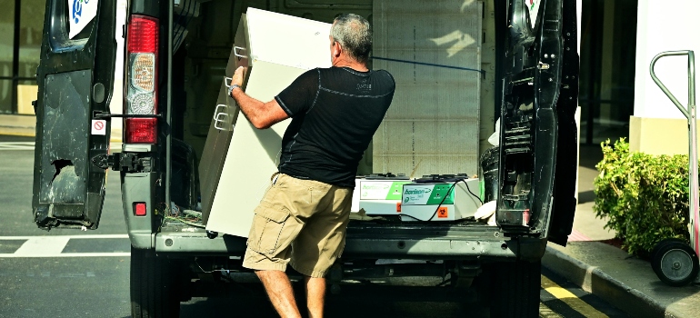 Mover lifting a large cabinet into a van as part of how to prepare furniture for moving safely.