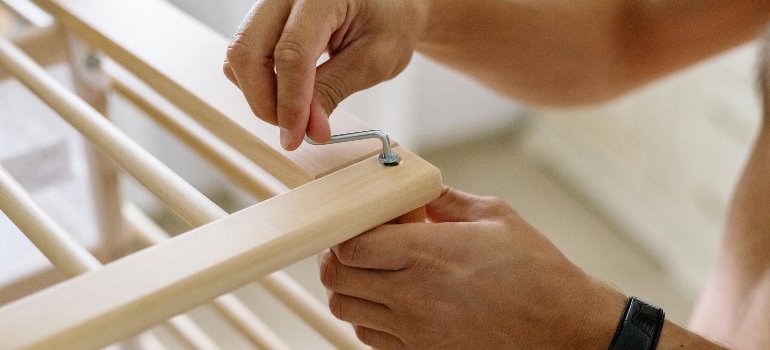 Person tightening furniture hardware with an Allen key during how to prepare furniture for moving and setup.