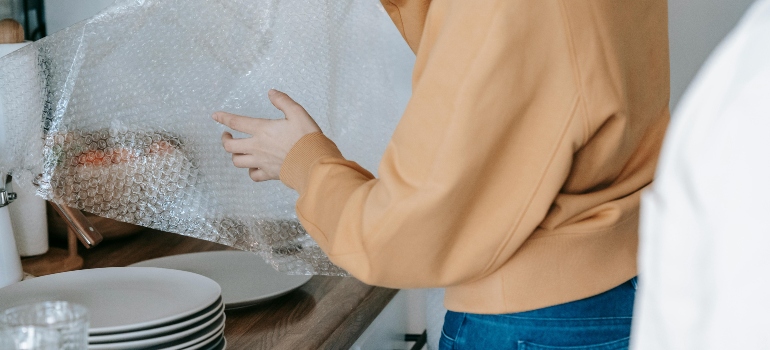 Person wrapping kitchen appliance in bubble wrap before packing for move.