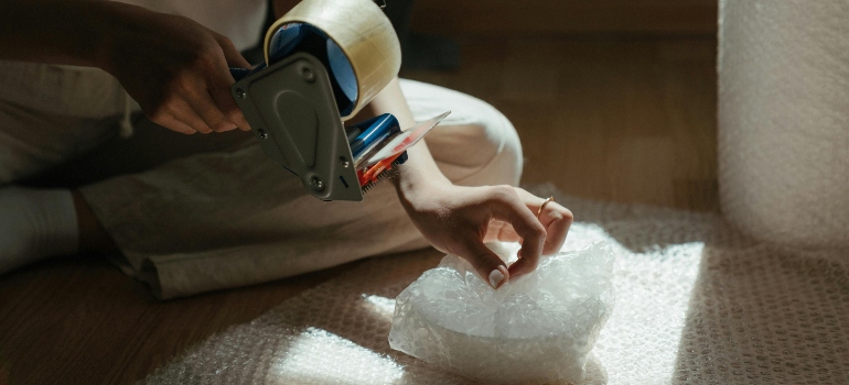 What are the types of packaging materials person using bubble wrap and tape.