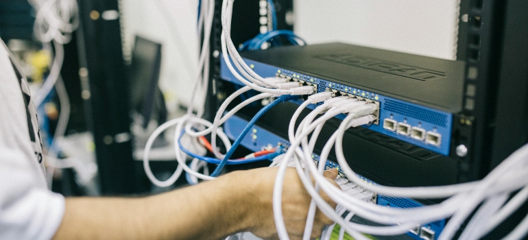 Technician connecting network cables in server rack during office relocation planning.