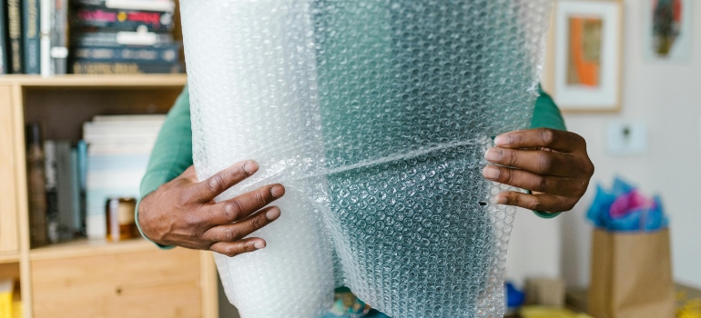 Hands using bubble wrap to pack wall art when moving and prevent damage